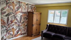 A room with a wooden cabinet, a dark sofa, a patterned rug, and a window with a view of a fence and trees.