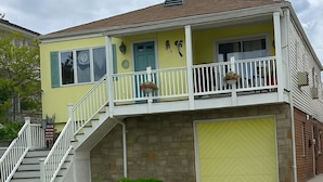 A two-story house with a yellow facade, a front porch, a staircase, and a garage.
