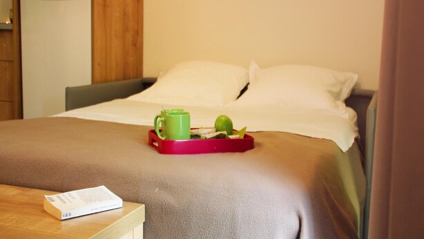 A hotel room with a bed, a bedside table with a book, and a tray with a green mug and an apple. - Beautiful Family Apartment in Amboise (Amboise)
