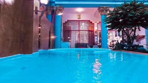 An indoor swimming pool with clear blue water, surrounded by columns and a decorative tree.