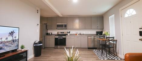 A modern kitchen with grey cabinets, a microwave, and a dining area with a black and white checkered rug.