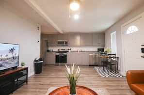Un salon moderne avec un téléviseur, une table basse en bois et un coin repas agrémenté d’un tapis à carreaux noirs et blancs.