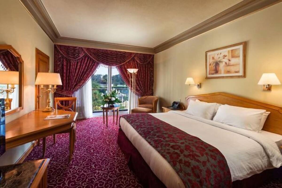 A hotel room with a bed, a desk, a chair, a table with flowers, and a view of the outdoors.