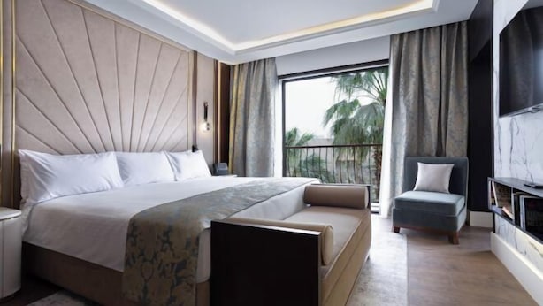 A modern bedroom with a large bed, a sofa, a TV, and a balcony with a view of palm trees. - Concorde El Salam Cairo Hotel & Casino (Cairo)