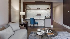 A modern hotel room with a sofa, a dining table with a tray of food, a blue chair, and a marble backsplash in the kitchen area. - Concorde El Salam Cairo Hotel & Casino (Cairo)