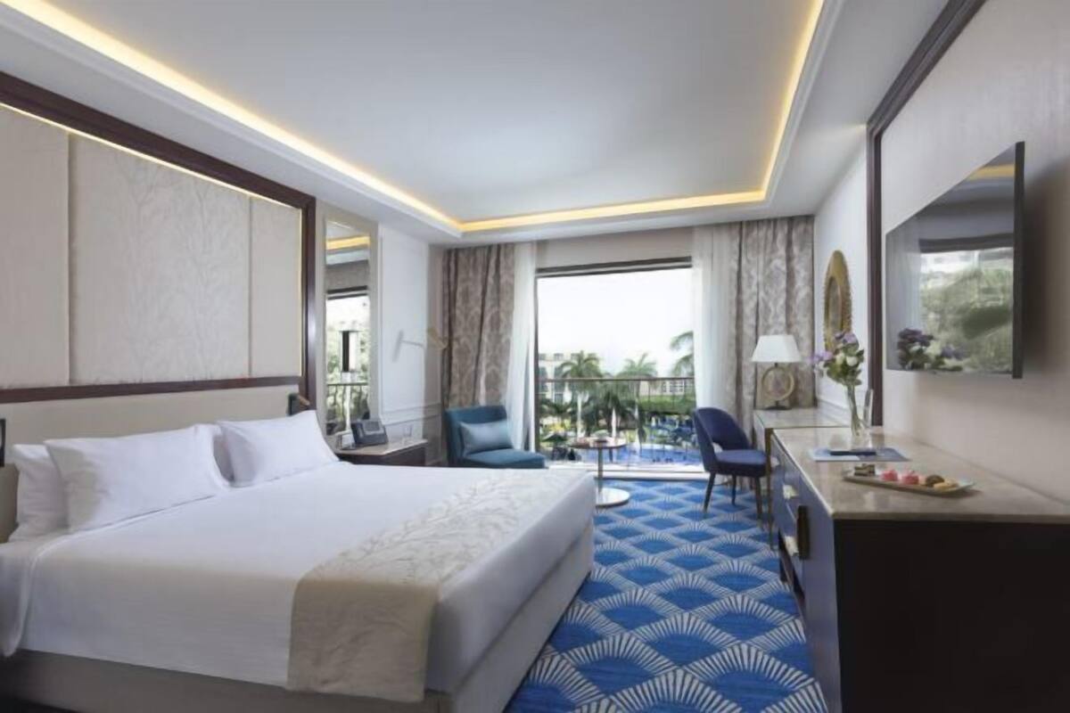 A hotel room with a large bed, a desk, a chair, a balcony with a view, and a large mirror.