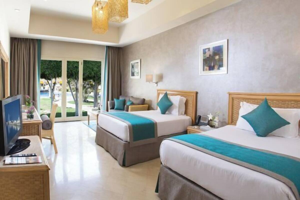 A hotel room with two beds, a desk with a computer, and a view of the outdoors.