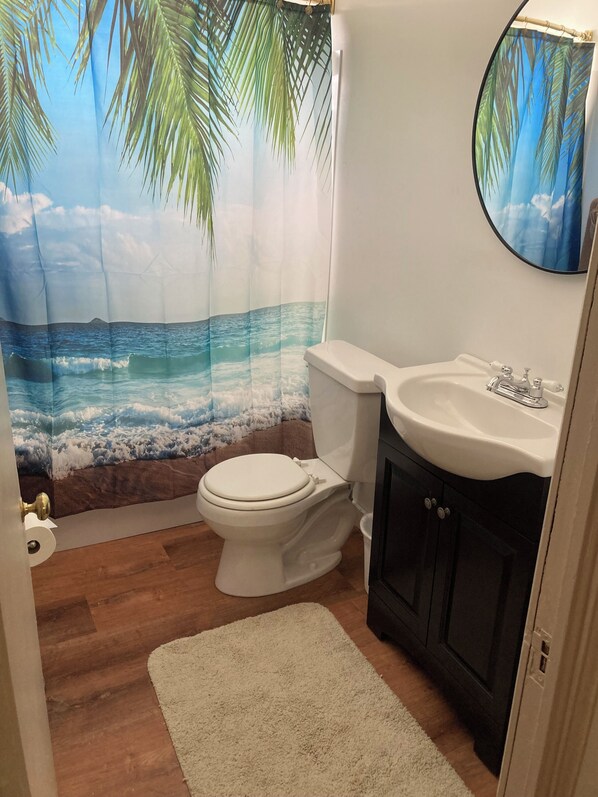 Un baño con inodoro, lavamanos y cortina de ducha con una escena de playa.