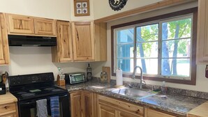 A kitchen with wooden cabinets, a black stove, a toaster, and a window with a view of trees.