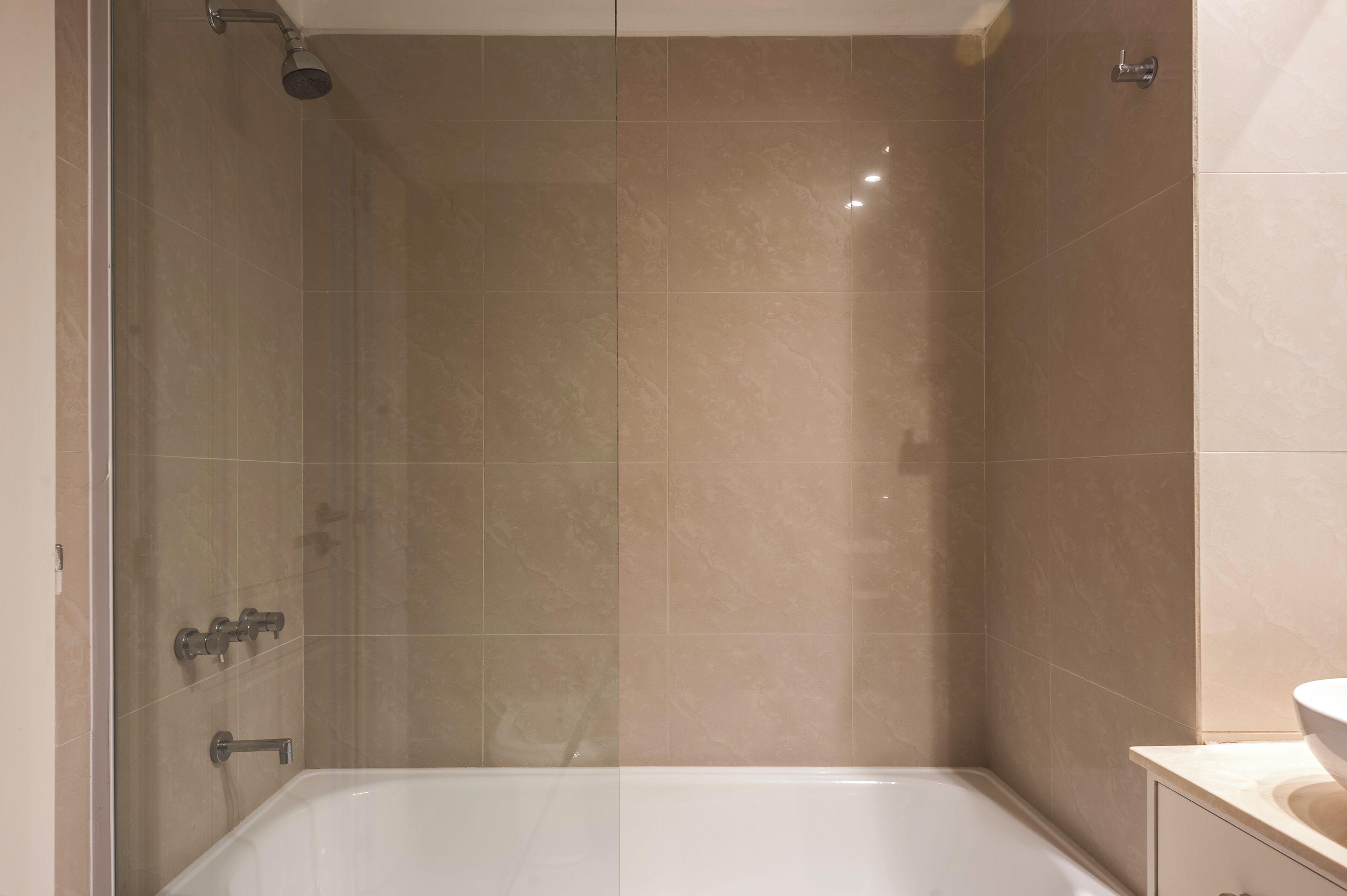 A modern bathroom with a glass-enclosed shower, beige tiles, and a white bathtub.