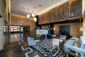A spacious lobby with a reception desk, seating area, and a large mural on the wall. - Barceló León Conde Luna (León)