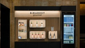 A B-Market gourmet display with shelves of snacks, wine, and bottled beverages, and a refrigerated display case. - Barceló León Conde Luna (León)