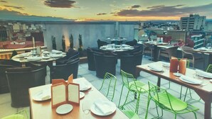 A rooftop restaurant with multiple tables and chairs, set against a cityscape during sunset. - Barceló León Conde Luna (León)