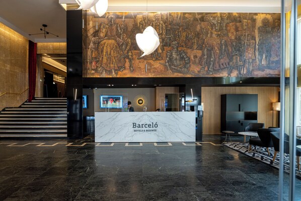 A modern hotel lobby with a marble reception desk, a large mural, and a staircase. - Barceló León Conde Luna (León)