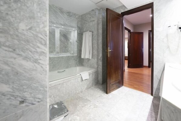 A bathroom with marble walls, a bathtub, a toilet, and a wooden door. - Barceló León Conde Luna (León)