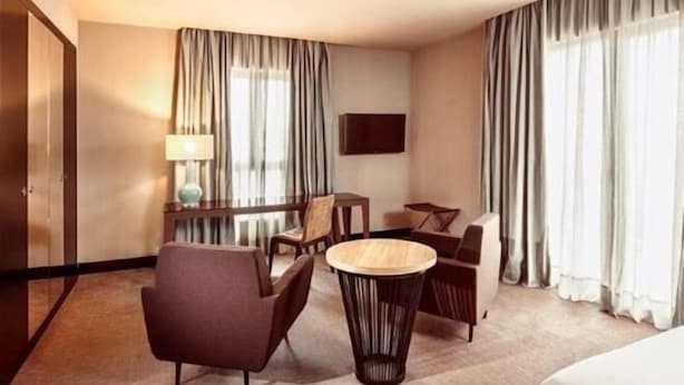 A hotel room with a bed, a desk, two chairs, a lamp, and a TV on the wall. - Barceló León Conde Luna (León)