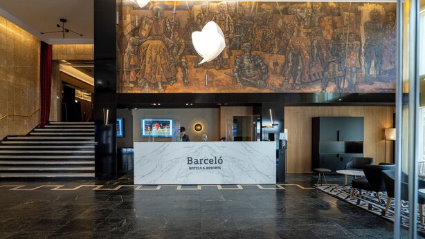 A modern hotel lobby with a marble reception desk, a large mural, and a staircase. - Barceló León Conde Luna (León)
