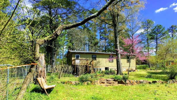 A rustic cabin with a wooden deck and a stone wall in a lush, green landscape. - Charming 3-bedroom house, WiFi, AC, in tranquil beautiful Russellville near Lake (Russellville)