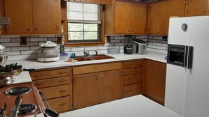 A kitchen with wooden cabinets, a white refrigerator, a coffee maker, and a window with blinds. - Charming 3-bedroom house, WiFi, AC, in tranquil beautiful Russellville near Lake (Russellville)