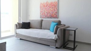 Un salon moderne avec un canapé gris, une petite table d’appoint et un tableau abstrait aux couleurs vives accroché au mur.