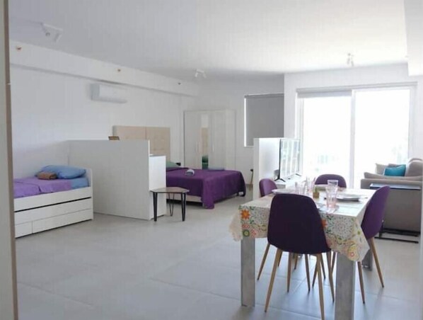 Een kleine kamer met een bed, een tafeltje en een zithoek met stoelen.