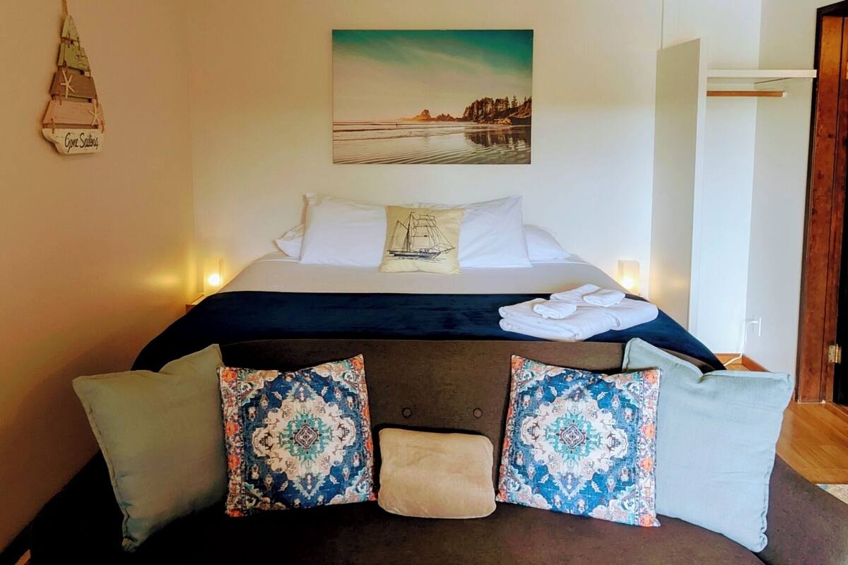 A bedroom with a bed, pillows, a rug, a painting, and a small wall decoration.
