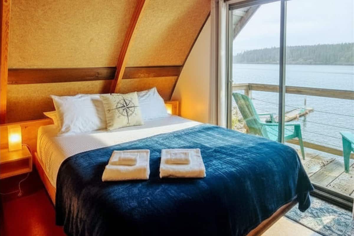 A bedroom with a large bed, a window with a view of a body of water, and a wooden ceiling structure.