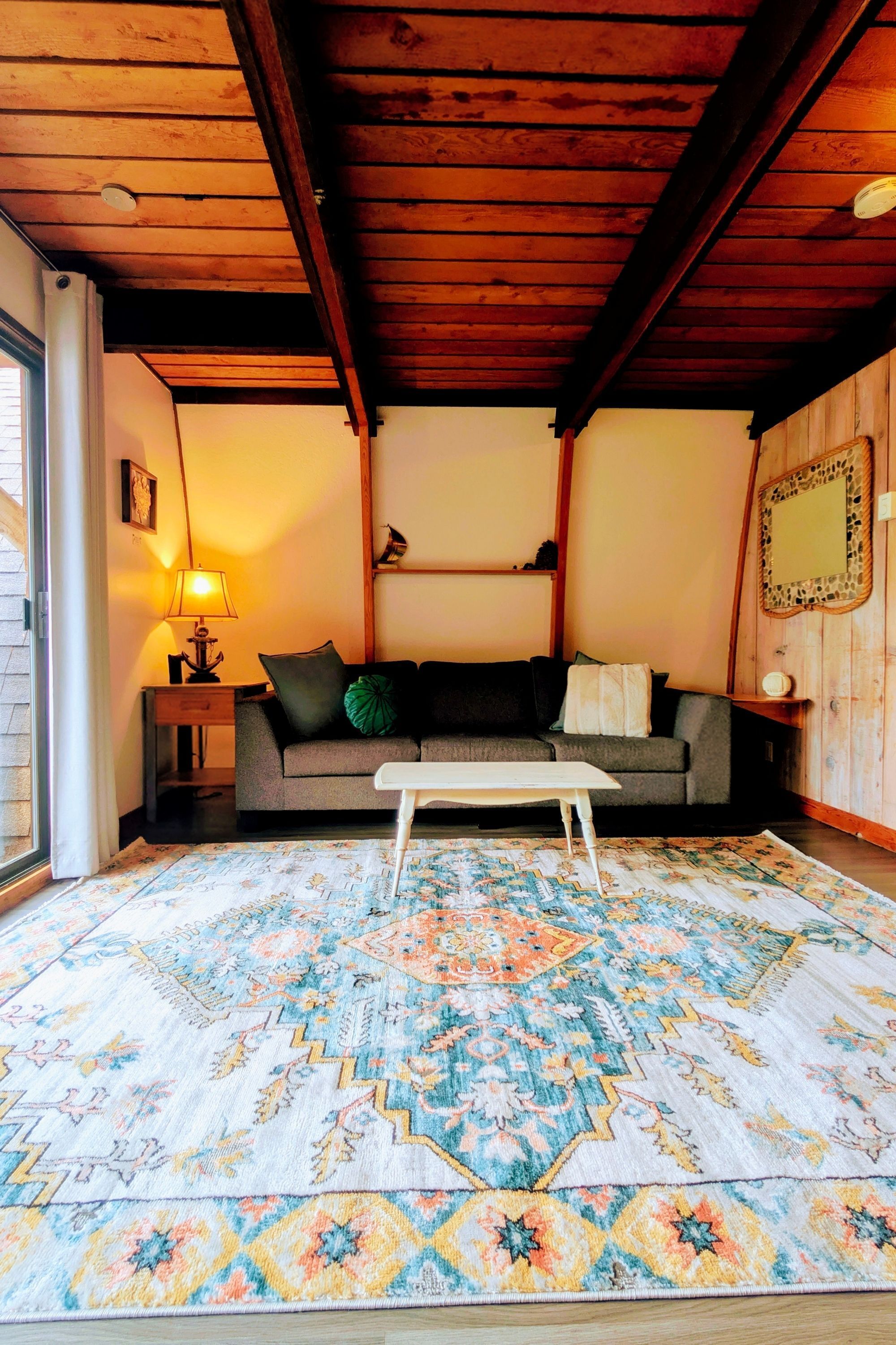 A cozy living room with a wooden ceiling, a sofa, a coffee table, and a patterned rug.