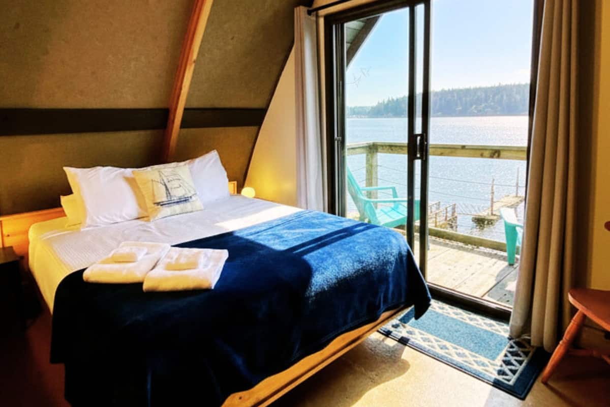 A bedroom with a bed, a view of the water, and a balcony.