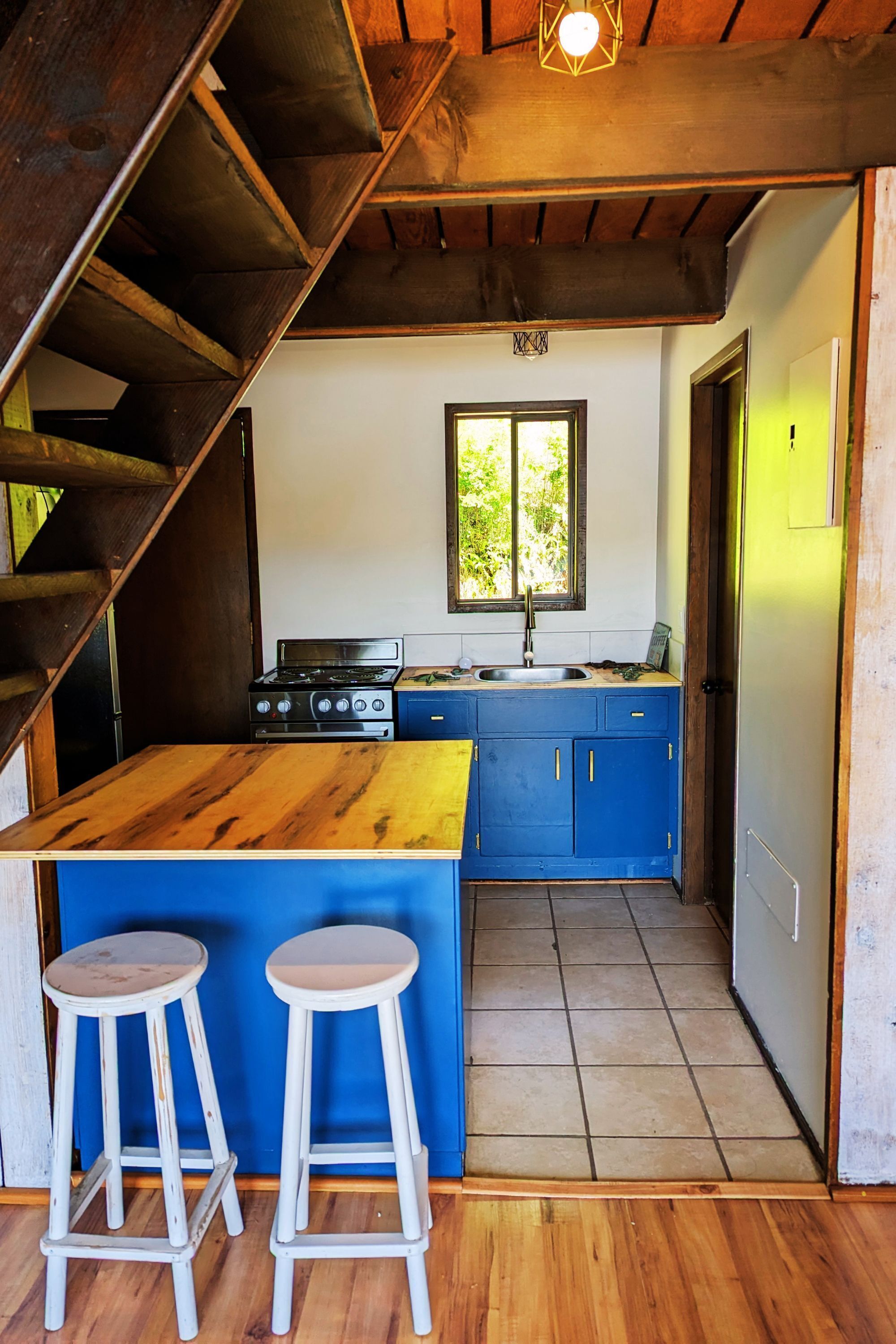 Een keuken met een houten kookeiland, blauwe kastjes, een fornuis en twee barkrukken.
