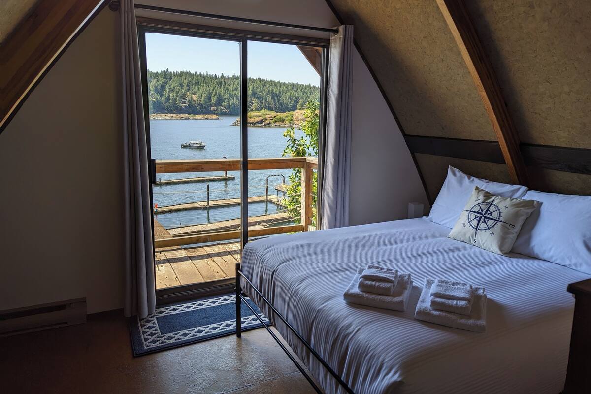 A bedroom with a bed, pillows, and a view of a lake and forest.
