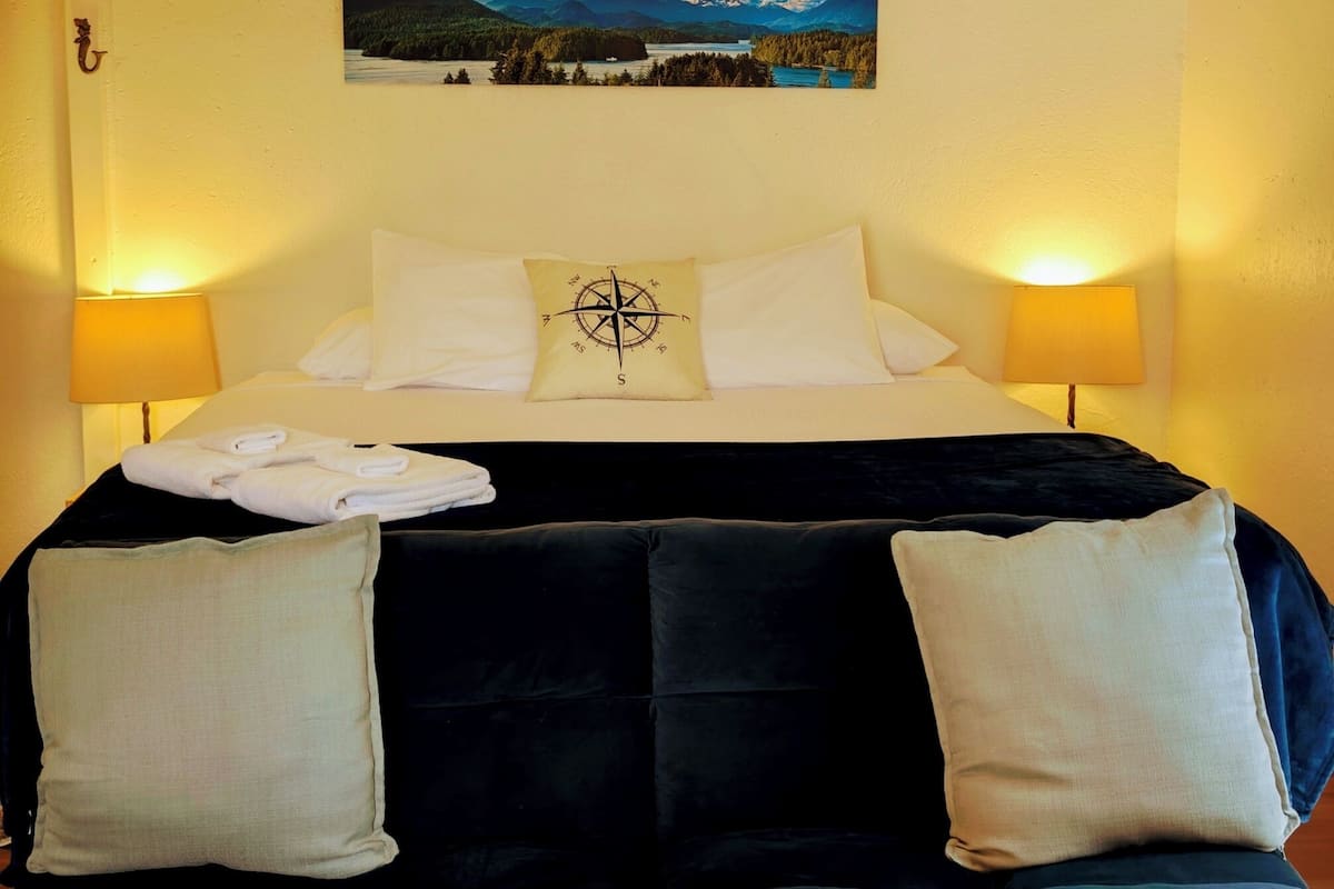 A hotel room with a bed, a wall-mounted painting, two bedside lamps, and a decorative pillow.