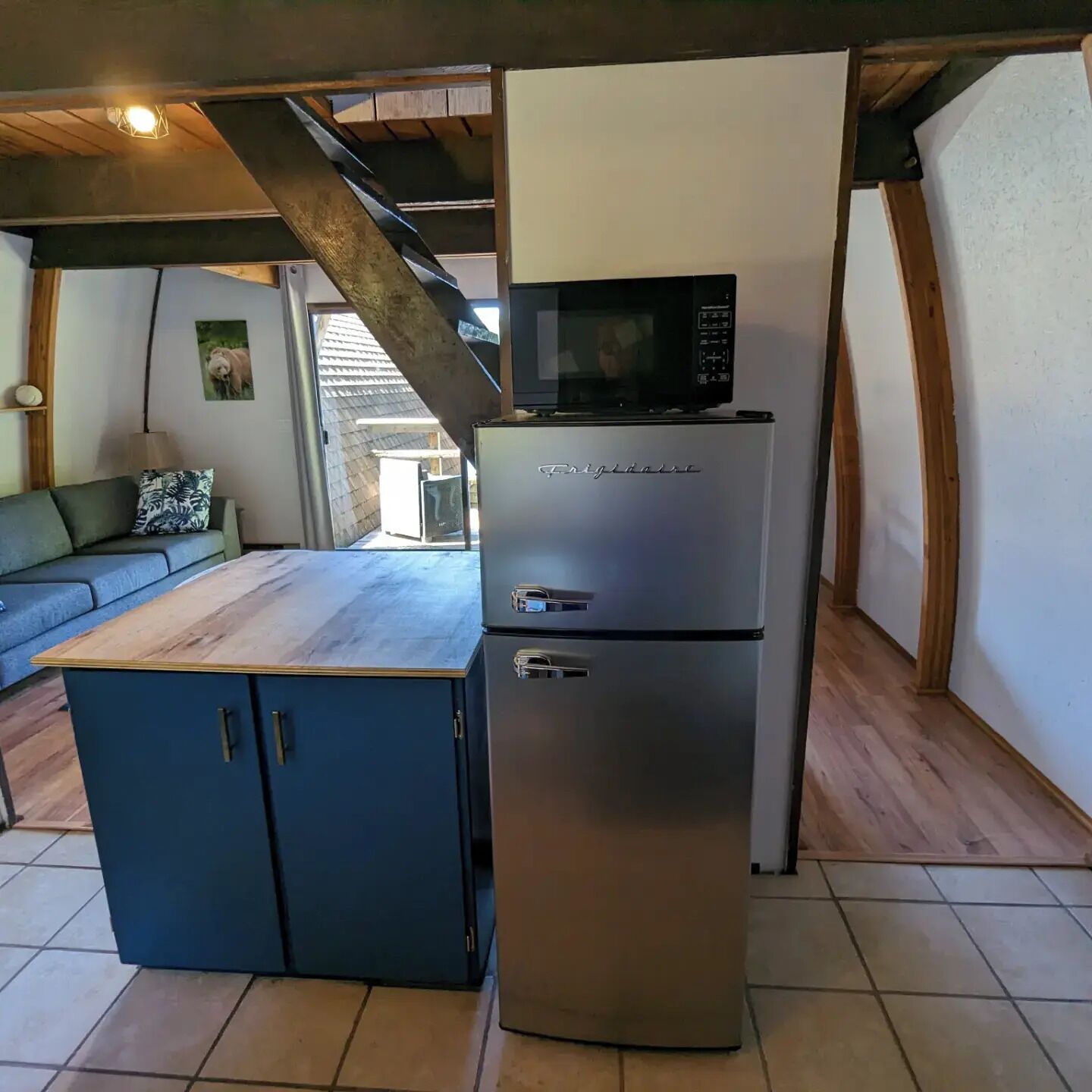 A compact kitchen with a refrigerator, microwave, and a wooden table.