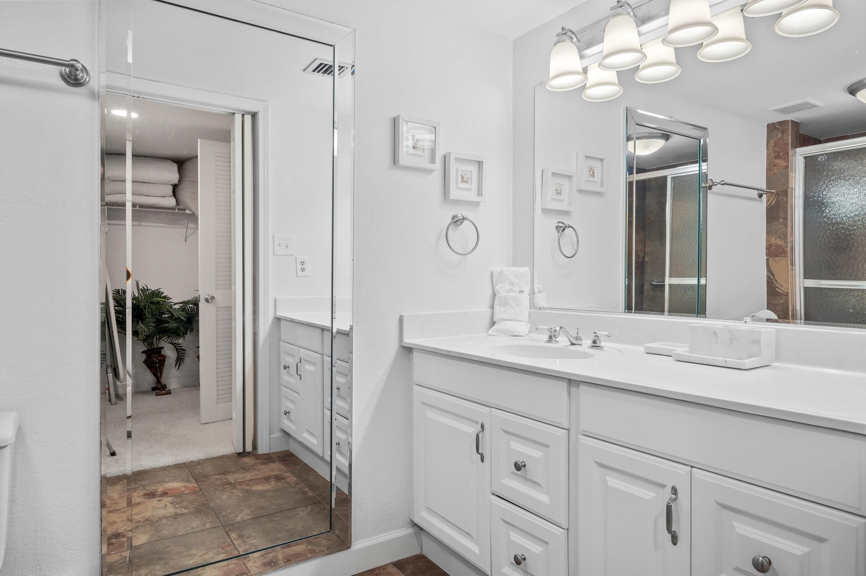 A modern bathroom with a large mirror, white cabinetry, and a glass shower enclosure.