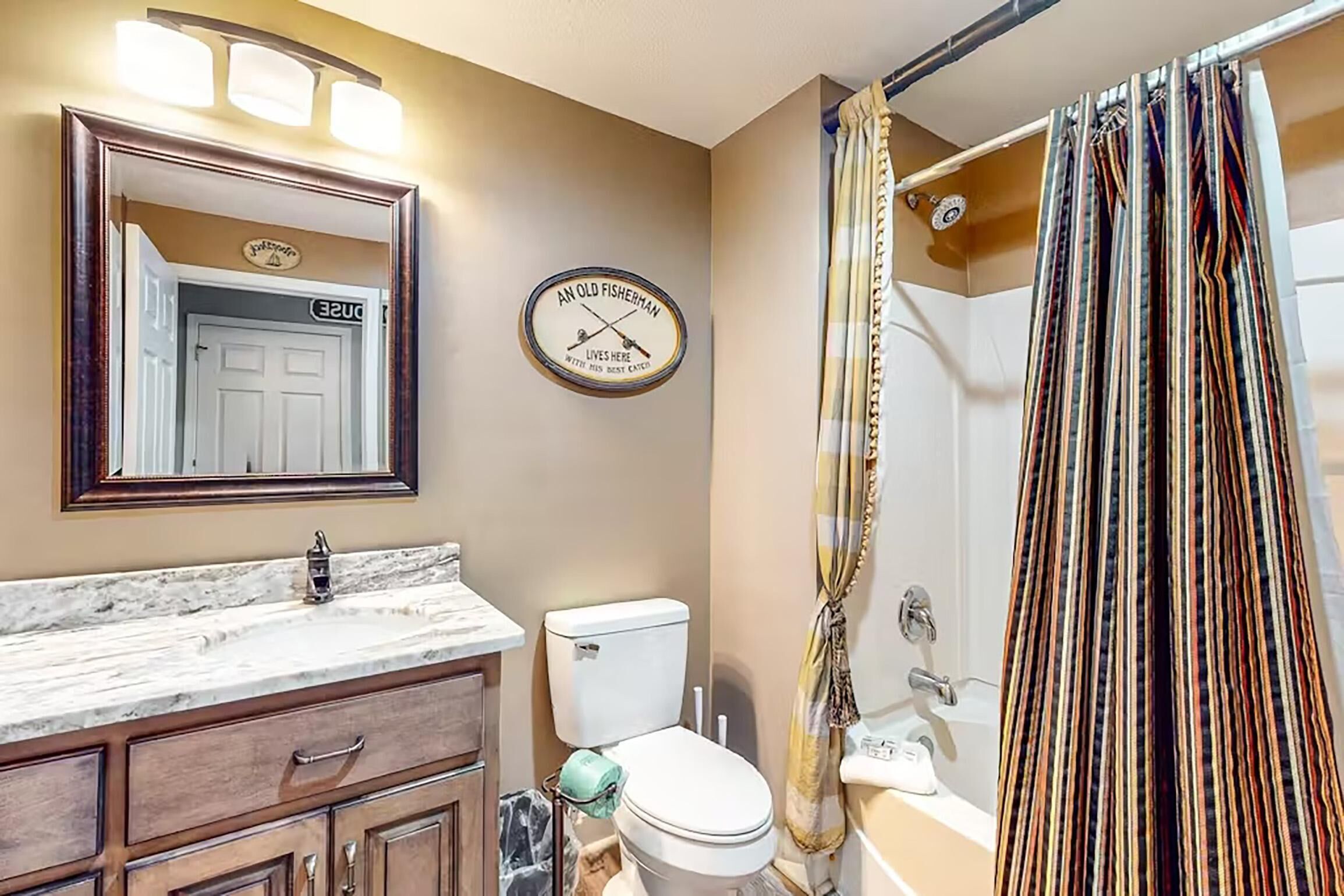 A bathroom with a marble sink, wooden vanity, a toilet, and a shower curtain.