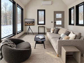 A modern living room with a large window, a sofa, a coffee table, and a chair. - Hust Haus | Sweeping Catskills Views on 20 Acres (Jeffersonville)