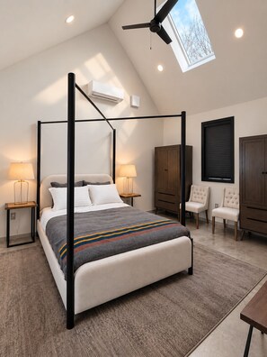 Une chambre à coucher avec un lit à baldaquin, un ventilateur de plafond, un appareil de climatisation et une fenêtre donnant sur la forêt.