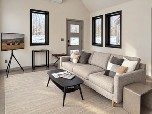 A living room with a sofa, coffee table, and a TV on a stand. - Hust Haus | Sweeping Catskills Views on 20 Acres (Jeffersonville)