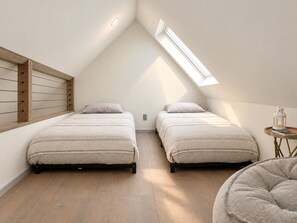 A small, well-lit room with two beds, a skylight, and a small table with a lantern. - Hust Haus | Sweeping Catskills Views on 20 Acres (Jeffersonville)