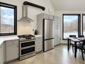 Une cuisine moderne équipée d’une cuisinière à gaz, d’un four, d’un réfrigérateur en acier inoxydable et d’un coin repas avec une table et des chaises.