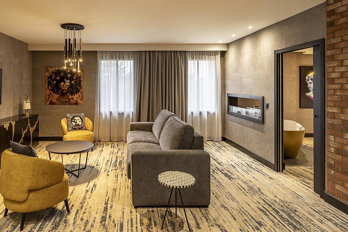A modern living room with a flat-screen TV, a sofa, a yellow armchair, a round coffee table, and a patterned rug.