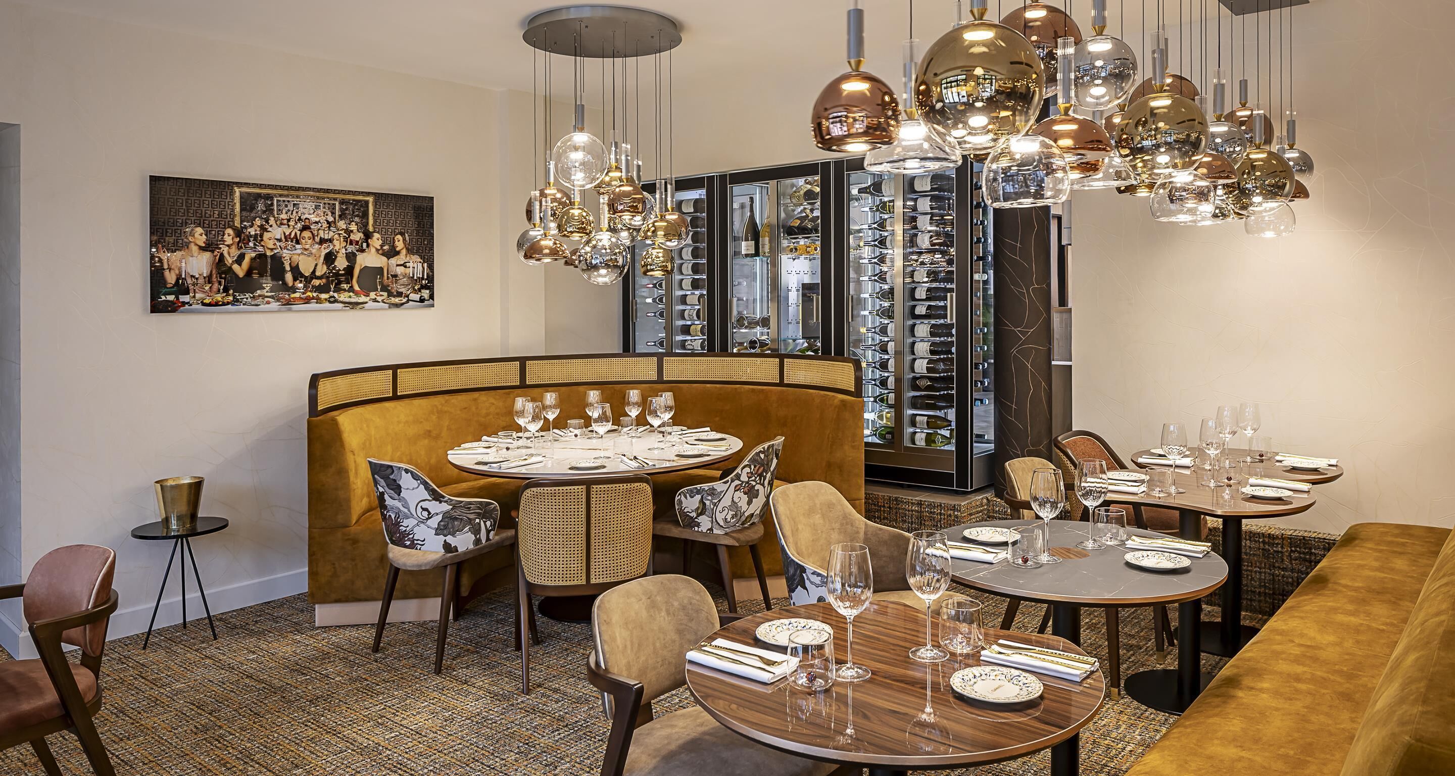 Un restaurant avec des tables rondes, des banquettes confortables et un présentoir à vin en arrière-plan.