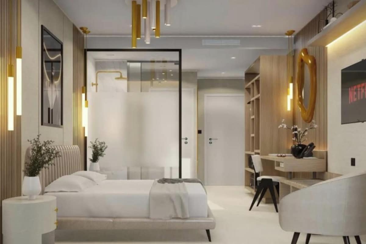 A modern bedroom with a bed, bedside tables, a desk, and a chair. There is a bookshelf and a wall-mounted TV.