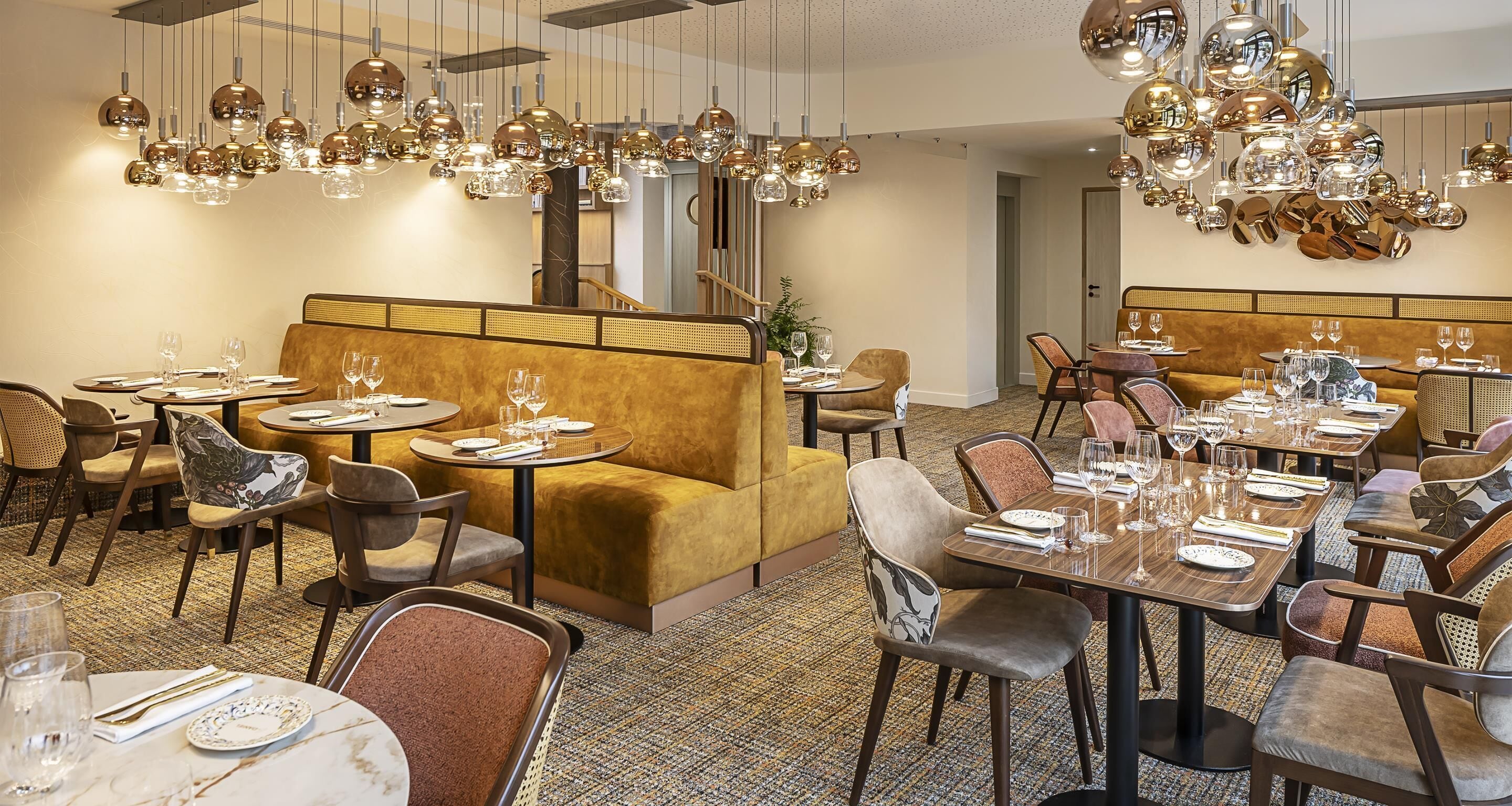 Un interior de restaurante con mesas redondas, asientos acolchados y lámparas esféricas colgantes.