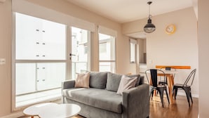 A modern living room with a grey sofa, a small white table, and a dining area with a wooden table and black chairs. - Premium y Moderno Recoleta A12J (Buenos Aires)
