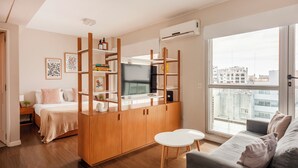 A modern apartment with a kitchenette, a bed, a sofa, and a large window offering a city view. - Premium y Moderno Recoleta A12J (Buenos Aires)