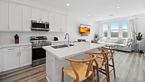 Una cocina moderna con armarios blancos, electrodomésticos de acero inoxidable y una isla central con taburetes de bar.