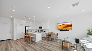 Una cocina moderna con armarios blancos, una isla central y un comedor con sillas de madera.