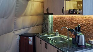 A compact kitchen with a stone backsplash, wooden cabinets, and a small sink. - Daxvalley Glamping (Tsalka)