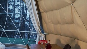 A dining area with a wooden table and red chairs, a bench, and a view of trees through a large window. - Daxvalley Glamping (Tsalka)